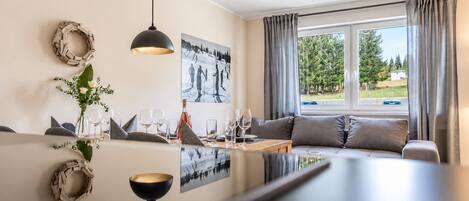 Ett modernt vardagsrum med en matplats, inrett med en soffa, ett soffbord och ett matbord med glas och en flaska.