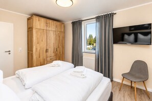 A hotel room with two beds, a wardrobe, a TV, and a chair.