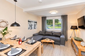 Ein modernes Wohnzimmer mit einer Couch, einem Esstisch für vier Personen, einem Couchtisch und einem an der Wand montierten Fernseher.