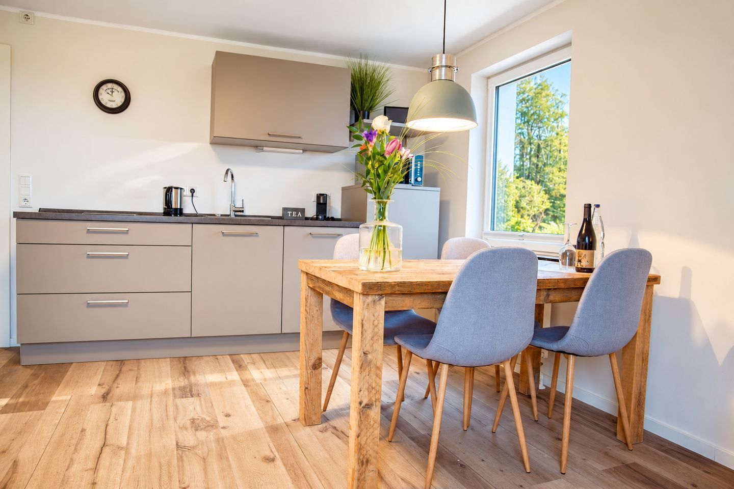 Una cocina moderna con una mesa de comedor de madera, sillas grises y una lámpara colgante.