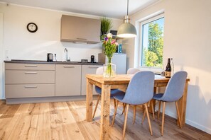 A modern kitchen with a wooden dining table, grey chairs, and a pendant light. - Smart Resorts - Haus Opal - Ferienwohnung 404 mit 1 Schlafzimmer, Max. 4 Personen - Smart Resorts (Winterberg)