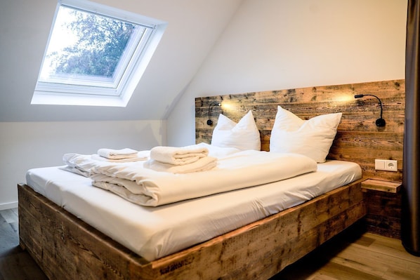 A bedroom with a wooden headboard, a skylight, and a neatly made bed with white linens and pillows.