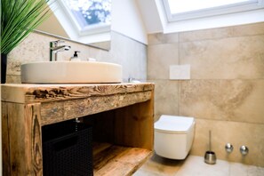 Une salle de bain avec un meuble-lavabo en bois, un évier, des toilettes et une fenêtre située au-dessus de l’évier.