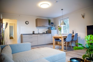 A modern kitchen with white cabinets, a dining area with a wooden table and chairs, and a cozy living space with a sofa.