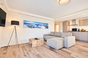 Een moderne woonkamer met een grijze bank, een houten bijzettafeltje en een vloerlamp.