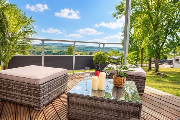 A balcony with wicker furniture, a glass table, and a view of the landscape.