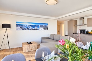 Een moderne woonkamer met een bank, een eettafel gedekt voor twee personen, en een groot landschap op de muur.