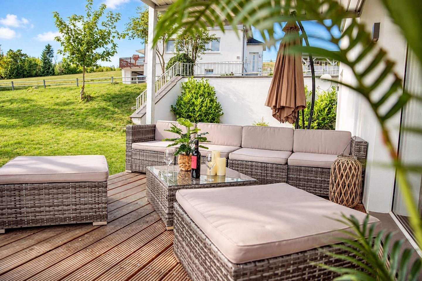 An outdoor seating area with wicker furniture, a glass table, and a bottle of wine.