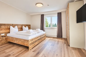 Een hotelkamer met een houten bed, witte lakens, een flatscreen televisie en een groot raam met gordijnen.