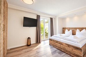 A bedroom with a large bed, a flat-screen TV mounted on the wall, and a view of the outdoors through a sliding glass door.