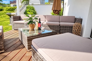 Een zonnig buitenterrein met rieten meubels, een tafel met glazen blad en een bloempot.