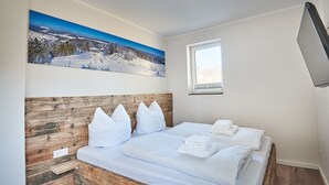 Makuuhuoneessa on puinen sängynpääty, valkoisilla lakanoiden peitetty sänky, ikkuna ja taulu, jossa on lumipeitteinen maisema.