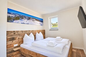 A bedroom with a wooden headboard, a bed with white bedding, a painting of a snowy landscape, a window with a view, and a flat-screen TV mounted on the wall. - Smart Resorts - Opal House - Apartment 402 with 1 bedroom and a balcony, (Winterberg)