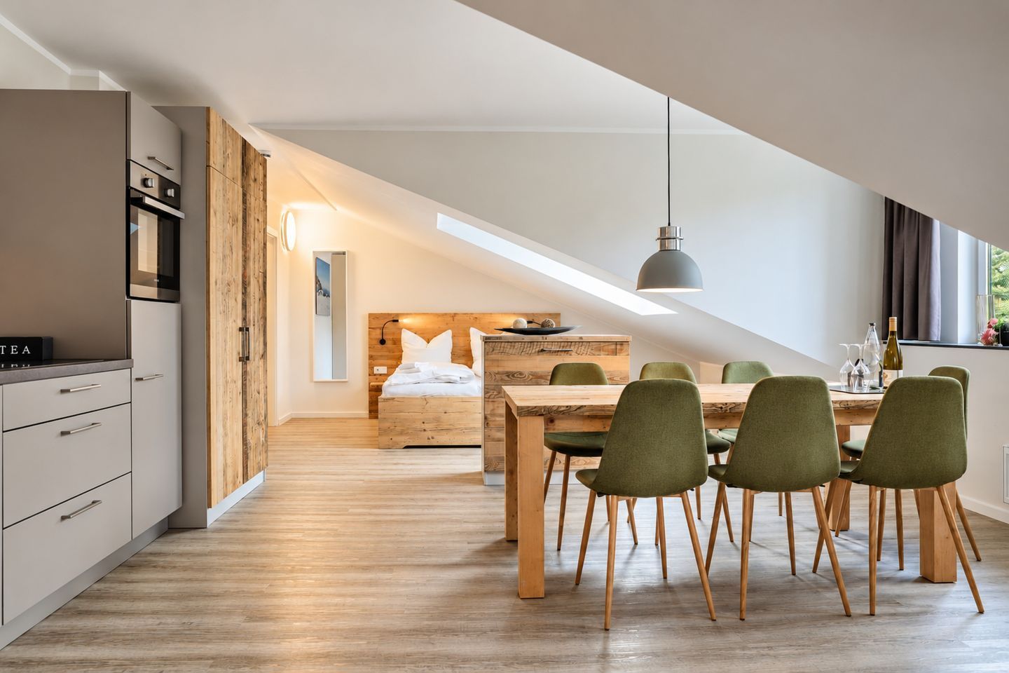 Une cuisine moderne avec un coin repas, une chambre à coucher aménagée en mezzanine avec une lucarne et une vue sur l’extérieur.