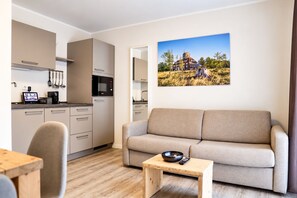Una sala moderna con un sofá, una pequeña mesa de madera y una zona de cocina con armarios y electrodomésticos.