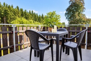 An outdoor patio with a table and chairs, surrounded by a wooden fence and trees.