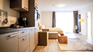 Een moderne keuken met een inbouwoven en magnetron, een eethoek met een houten tafel en stoelen, en een woonkamer met een bank en salontafel.
