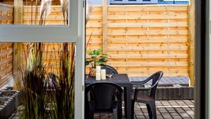 Een terras buiten met een houten omheining, een tafel met stoelen en een bloempot.