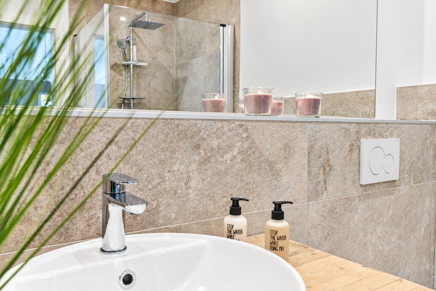 A modern bathroom with a white sink, a handheld showerhead, and two soap dispensers.