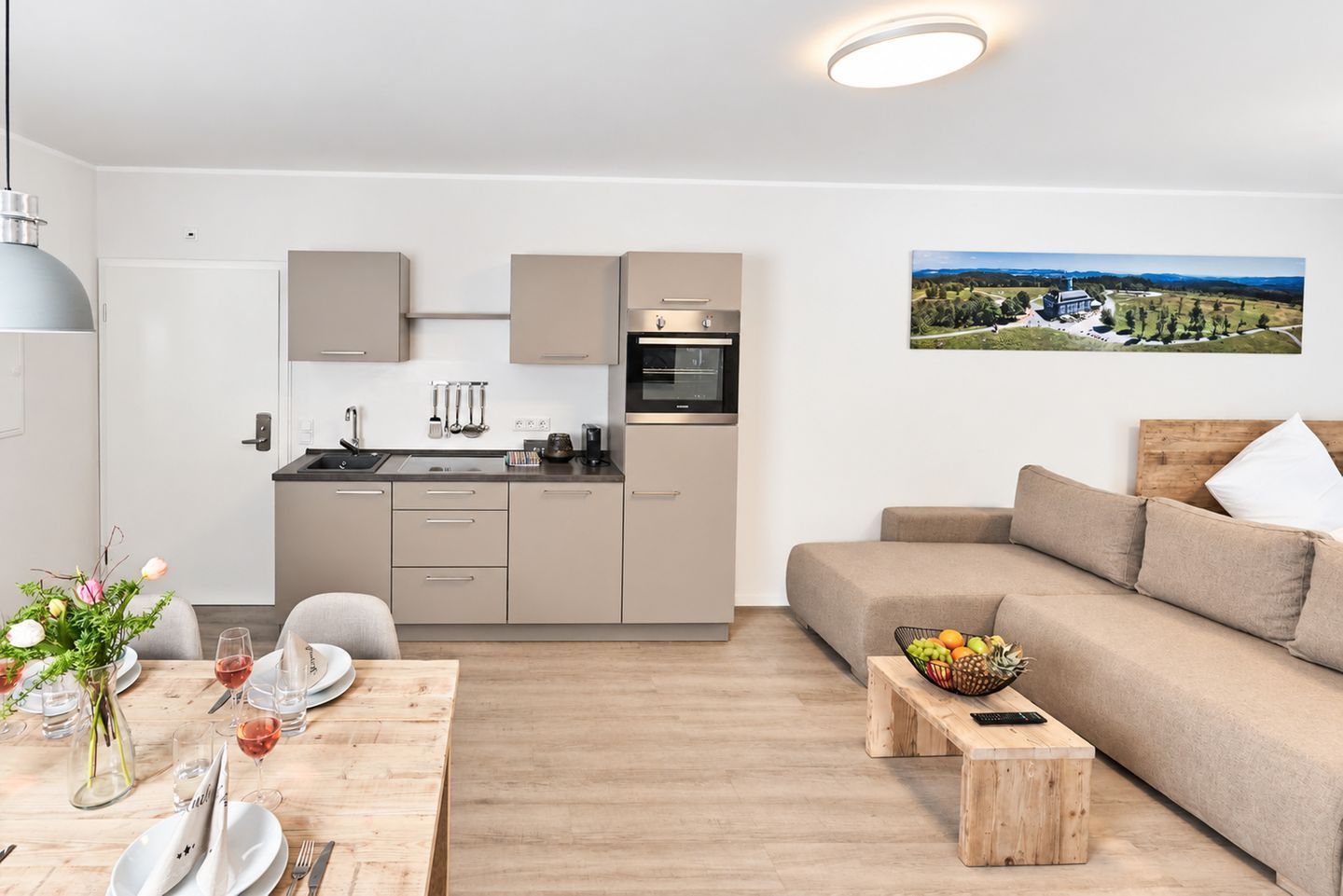 Un appartement moderne comprenant un coin cuisine, un espace repas avec une table en bois et un salon avec un canapé et un tableau.