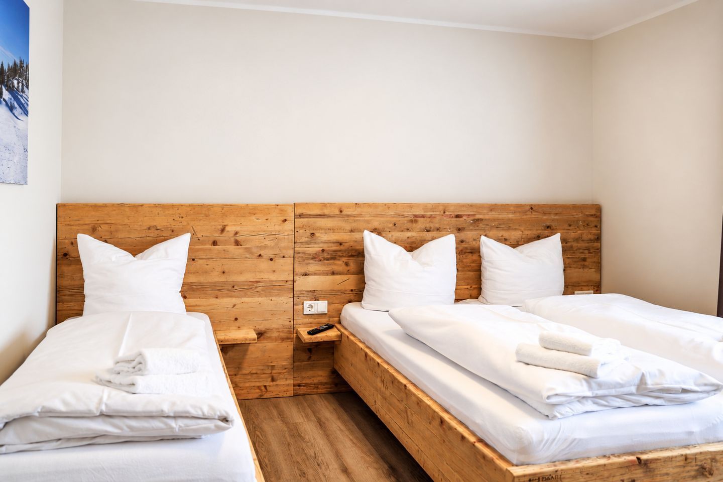 Een hotelkamer met twee enkele bedden, houten hoofdborden, wit beddengoed en een klein nachtkastje met een afstandsbediening.