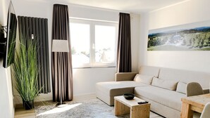 Un salon moderne avec un canapé, une table basse, un téléviseur et une grande fenêtre avec des rideaux.