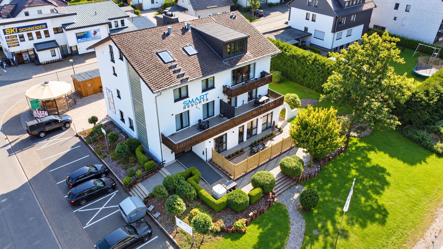 A modern two-story building with a balcony on the second floor, surrounded by well-maintained gardens and a parking area.