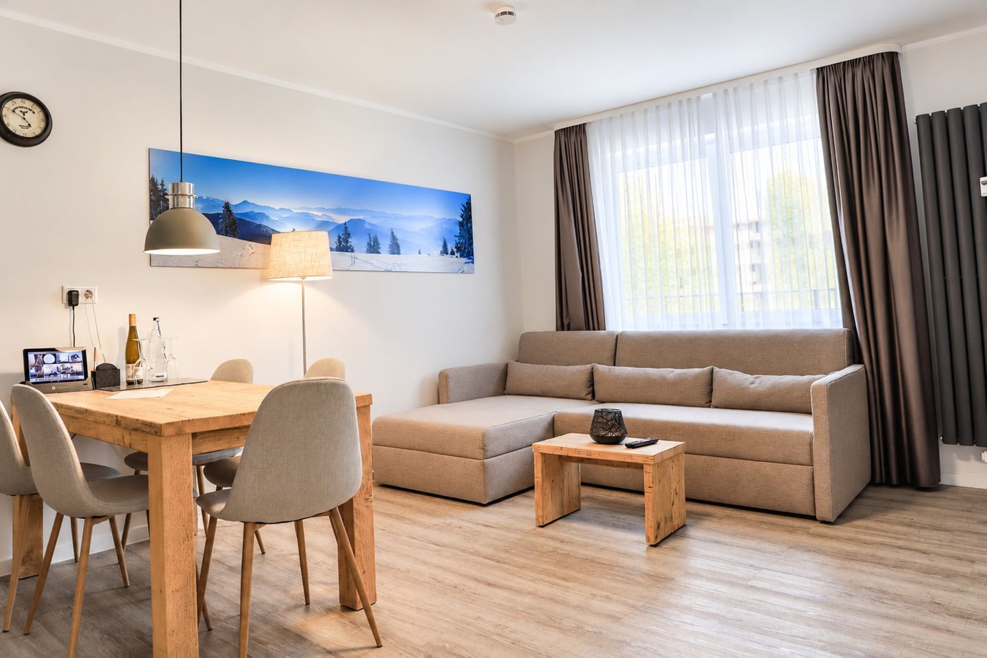 Un salon moderne avec une table à manger en bois, un canapé beige et un tableau représentant un paysage de montagne.