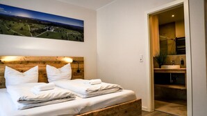 Een netjes opgemaakt bed met witte lakens, een houten hoofdbord en een schilderij van een sterrenhemel erboven.