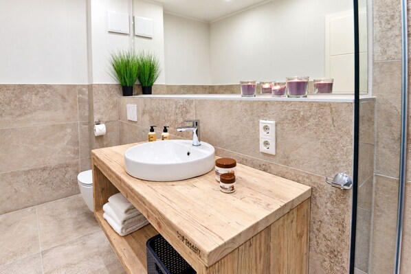 A modern bathroom with a wooden vanity, a white sink, and a glass shower enclosure.