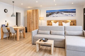 A modern living room with a grey sofa, wooden dining table, and a painting of a snowy landscape.
