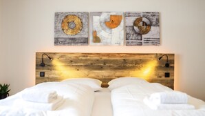 A bed with white linens, a wooden headboard, and three abstract paintings above it.