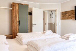 Une chambre d’hôtel avec deux lits, une armoire en bois, une porte donnant sur une salle de bain et une horloge fixée au mur.