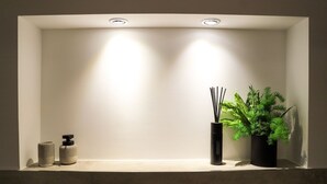 A bathroom vanity with a white countertop, two bottles of hand soap, a black diffuser with reed sticks, and a potted plant.