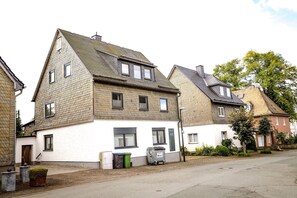 A two-story house with a white facade, multiple windows, and a visible trash bin.