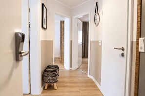 Ein Flur mit weißen Türen, Holzboden, einem kleinen gemusterten Hocker und einer Wanduhr.