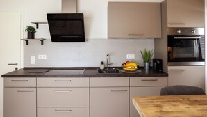A modern kitchen with a built-in oven, a microwave, and a stainless steel range hood. There is a sink with a faucet, a countertop with a fruit bowl, and a potted plant.