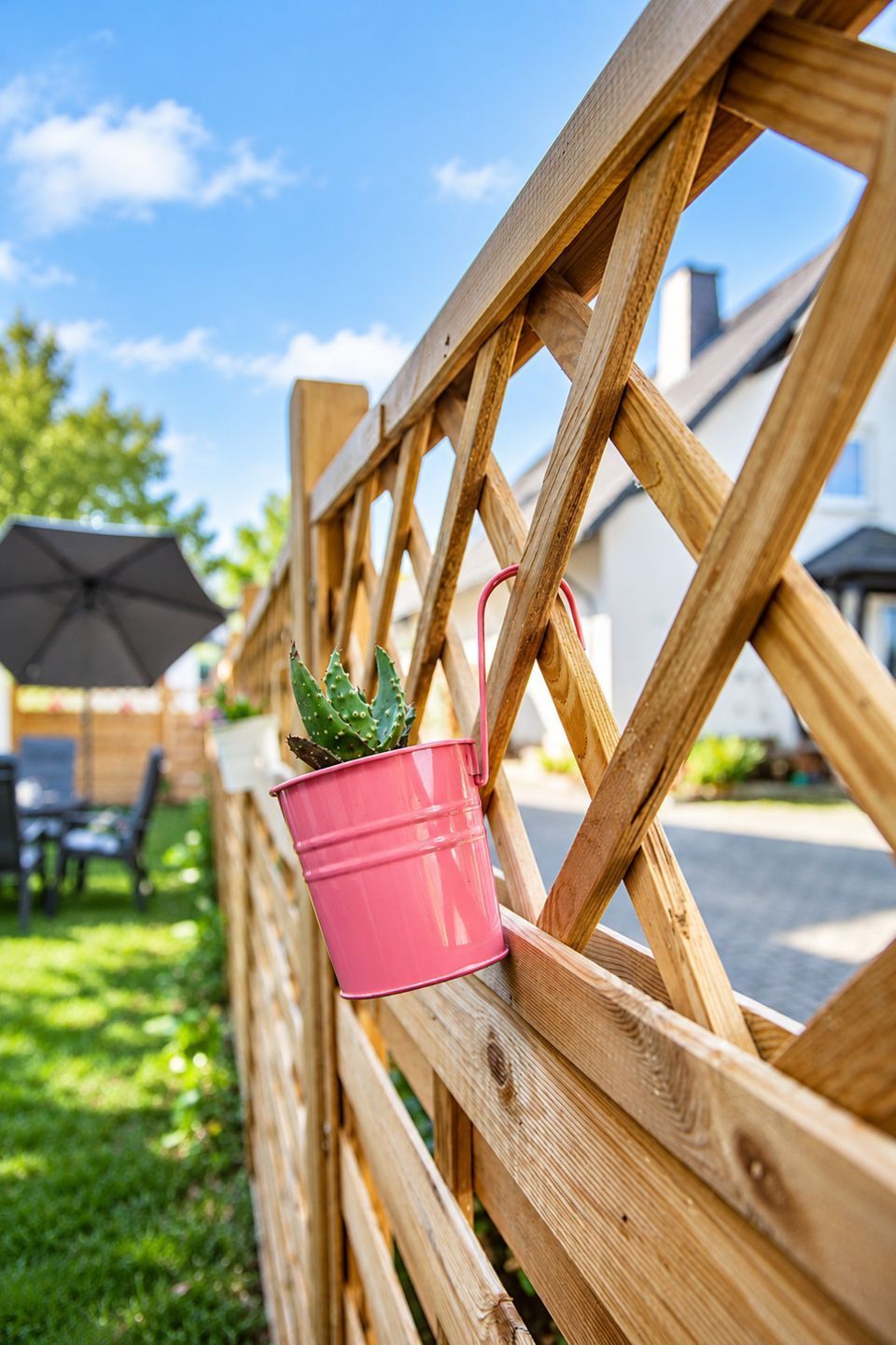 A wooden fence with a pink metal pot containing a cactus.
