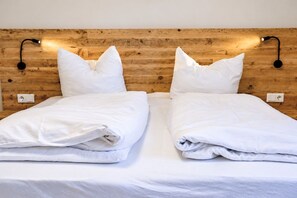 Cama doble con ropa blanca, dos almohadas y cabecero de madera con luces fijadas a la pared.
