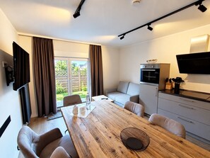 Una sala de estar moderna con una mesa de comedor de madera, asientos cómodos, un horno empotrado y un televisor de pantalla plana montado en la pared.