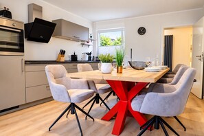 Una cocina moderna con comedor, que incluye una isla central, sillas tapizadas de gris y una mesa con base roja.