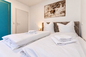 A hotel room with two beds, white linens, a mounted deer photograph, and a teal-colored wardrobe.