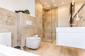 Un baño moderno con ducha envuelta en vidrio, inodoro blanco y tocador blanco.