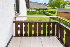 A balcony with a wooden railing and a view of a well-maintained garden and houses in the background. - Smart Resorts - Haus Rubin - Ferienwohnung 107 mit 2 Schlafzimmern und Balkon, Max. 6 Personen - (Winterberg)