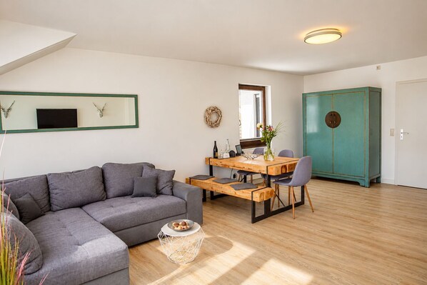 Una sala moderna con un sofá gris, una mesa de comedor de madera y un mueble de baño color turquesa.