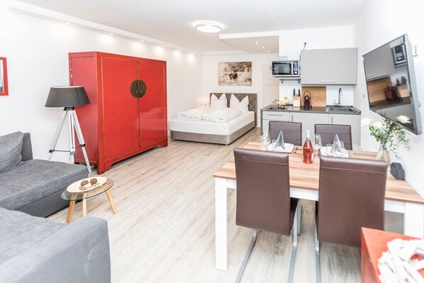 Une chambre d’hôtel moderne comprenant un coin repas, une armoire rouge, un lit et une kitchenette.