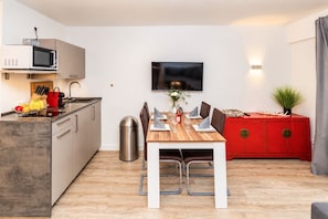 A compact living space with a kitchenette, dining area, and a red cabinet with a plant. - Smart Resorts - Haus Rubin - Studio-apartment 102 mit Terrasse, Max. 4 Personen - Smart Resorts Haus (Winterberg)