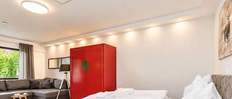 A modern bedroom with a bed, a red wardrobe, a sofa, and a floor lamp.