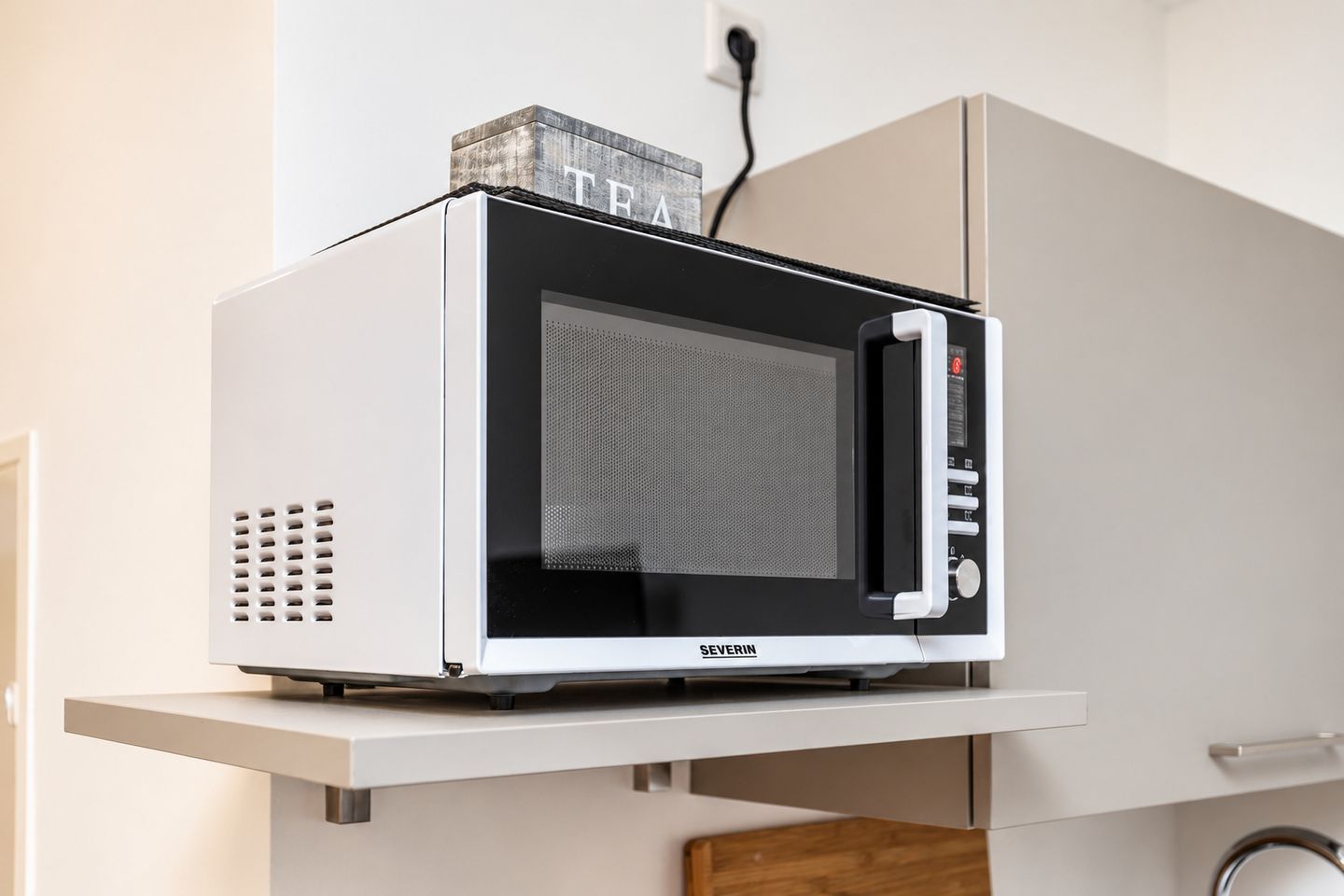 A microwave oven on a white shelf in a kitchen.