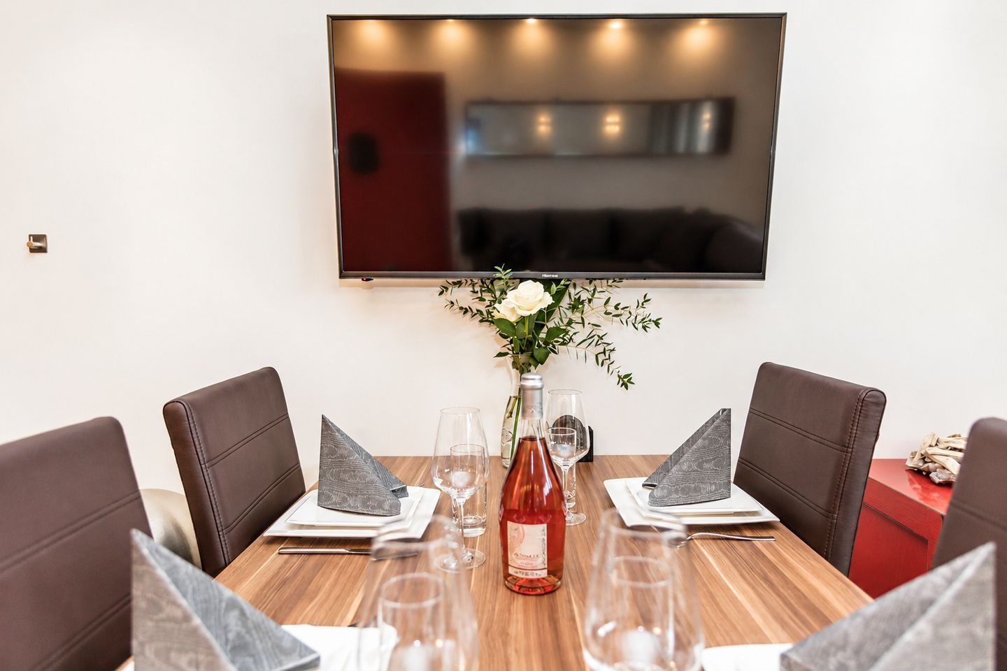 A dining table with four chairs, a vase with flowers, and a bottle of wine.